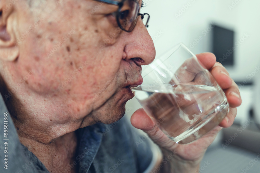 Senior man drinking a glass of water with a happy face and looking at camera. Portrait of a senior man relaxing at home and drinking water. Senior man drinking a glass of water with a happy face and looking at camera. Portrait of a senior man relaxing at home and drinking water.