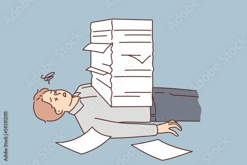 Stressed man lying under paperwork pile 