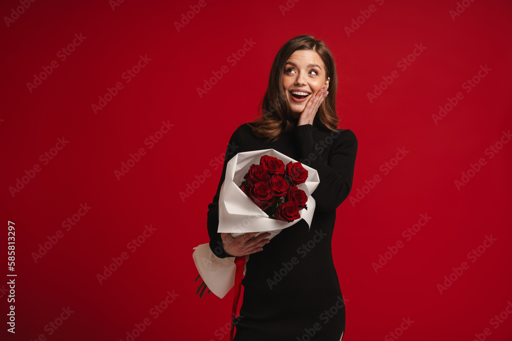 Smiling woman holding bouquet of roses and touching her cheek isolated over red background Smiling woman holding bouquet of roses and touching her cheek isolated over red background