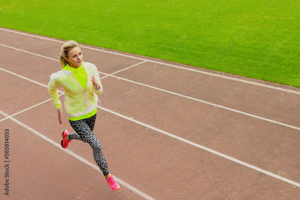 A young woman in a bright tracksuit runs on a treadmill at an outdoor stadium