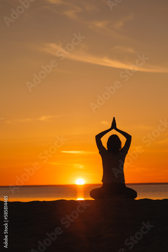 yoga meditation, silhouette of woman at sunset in lotus position. health recreation and sports, outdoor training. poster, postcard. person is engaged in breathing practices on seashore. mental health