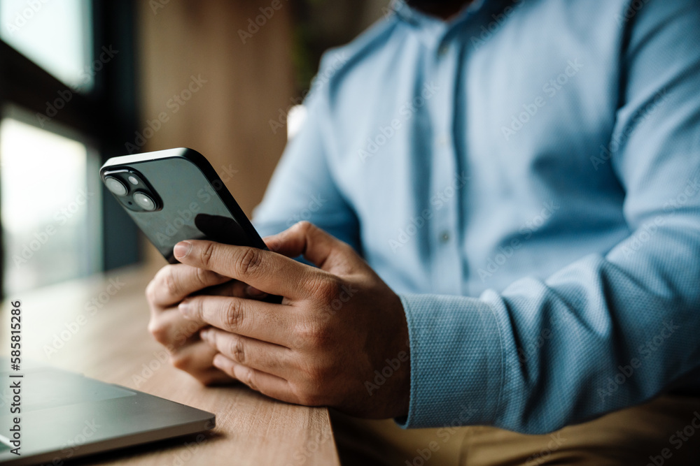 Close up of male hands using smartphone while sitting at table indoors Close up of male hands using smartphone while sitting at table indoors
