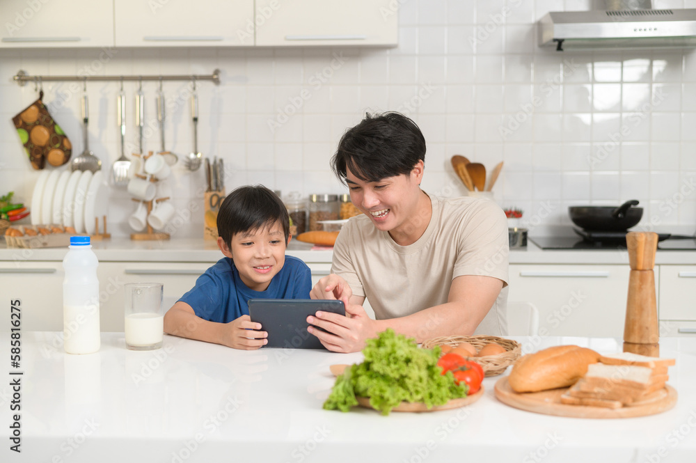 Young Asian father and his son using digital tablet enjoying together in kitchen at home Young Asian father and his son using digital tablet enjoying together in kitchen at home