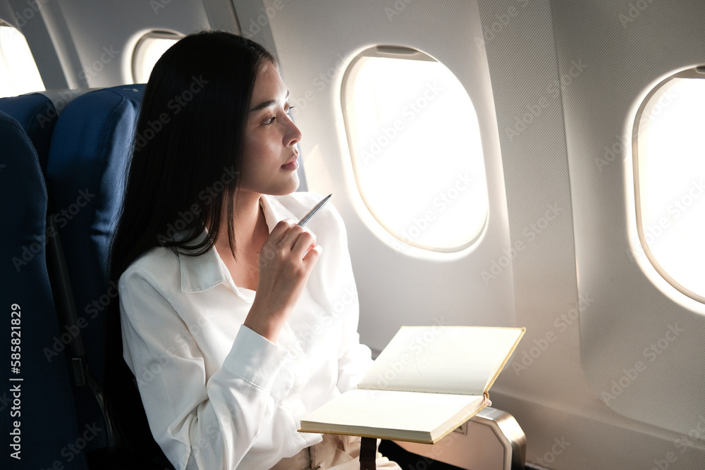 Successful beautiful young asian business woman sits in airplane cabinplane and works on digital tablet with stylus. Flying at first class.