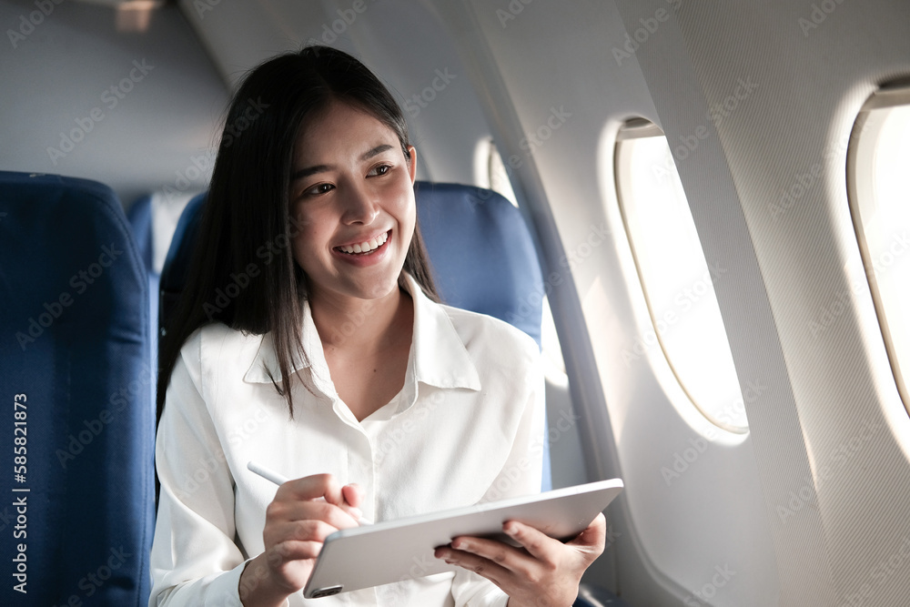 Joyful asian woman sits in the airplane and using tablet while go to travel Joyful asian woman sits in the airplane and using tablet while go to travel