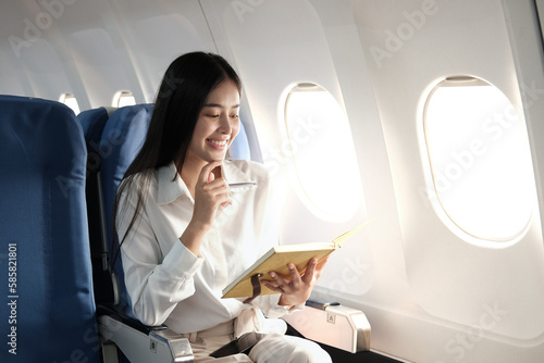 portrait of A successful asian business woman or female entrepreneur in formal suit in a plane sits in a business class seat and uses smartphone with documents for work during flight