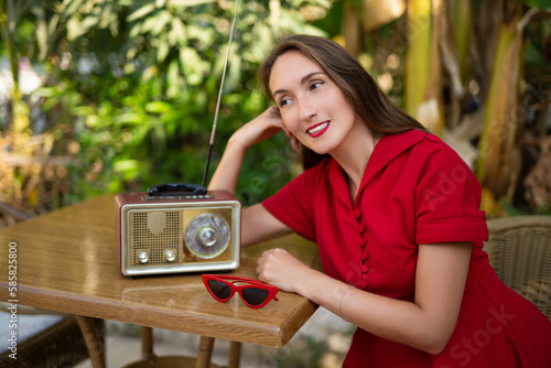 a beautiful girl in a red retro style dress listens to an antique radio.