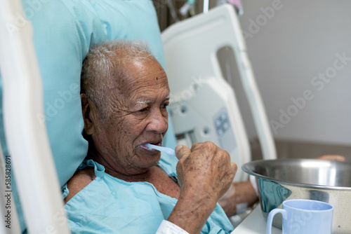 inpatient man brushing teeth for mouth hygiene on patient bed in hospital, a senior try to focus on clean his teeth after meal from modern medical treatment, old guy concentrate with daily mouth care.