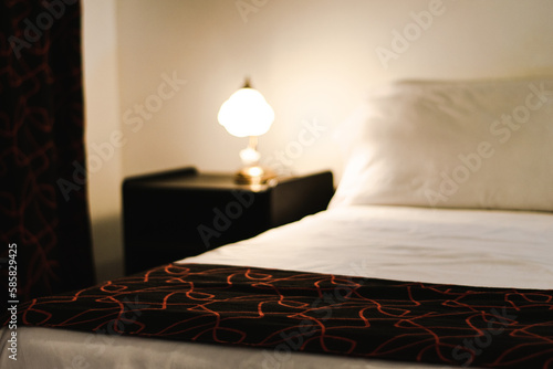 Night table with lamp besides bed out of focus