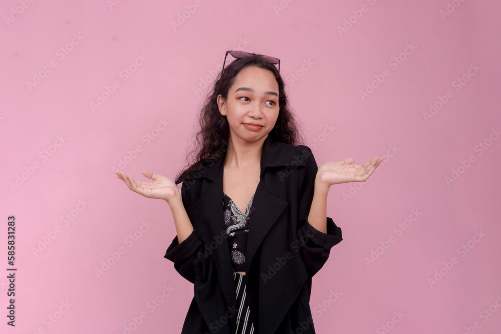 An undecided and frustrated woman does not know what to do. Shrugging and smirking. Isolated on a light pink background. An undecided and frustrated woman does not know what to do. Shrugging and smirking. Isolated on a light pink background.