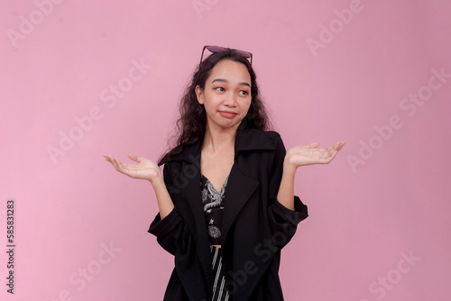 An undecided and frustrated woman does not know what to do. Shrugging and smirking. Isolated on a light pink background. photo