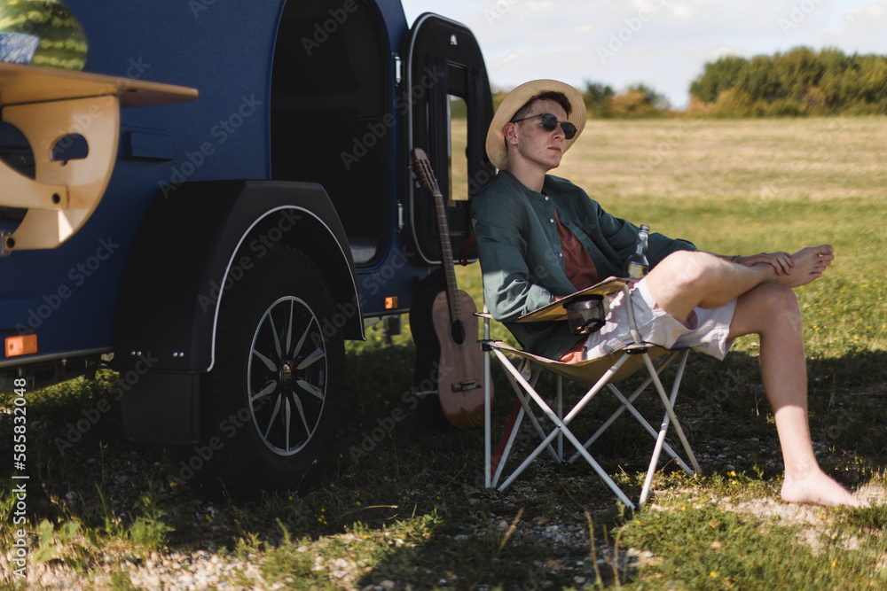 Naklejka premium Young man sitting in front of van enjoying summer time.