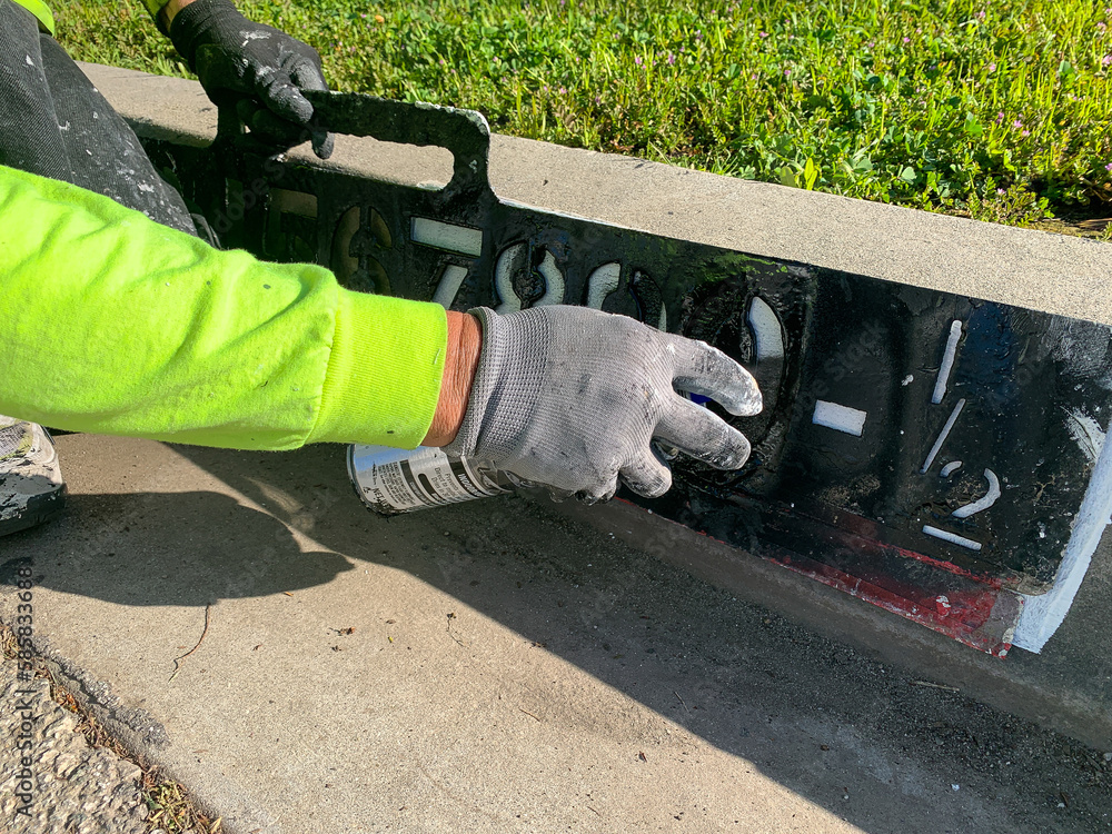 City worker painting address on street curbs using stencil numbers with