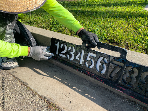 City worker painting address on street curbs using stencil numbers with white and blank paint
