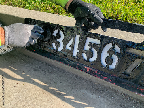 City worker painting address on street curbs using stencil numbers with white and blank paint
