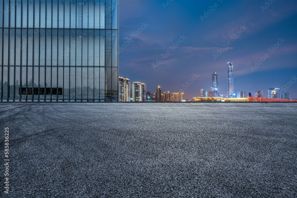 Asphalt road and glass wall with city skyline at night Asphalt road and glass wall with city skyline at night