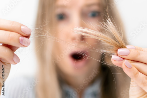 Upset blond woman holds the fallen hair with damaged brittle dry split ends in her hand in front of her face, her mouth wide open in shock, close-up. Health care and haircare, hairloss problem. photo