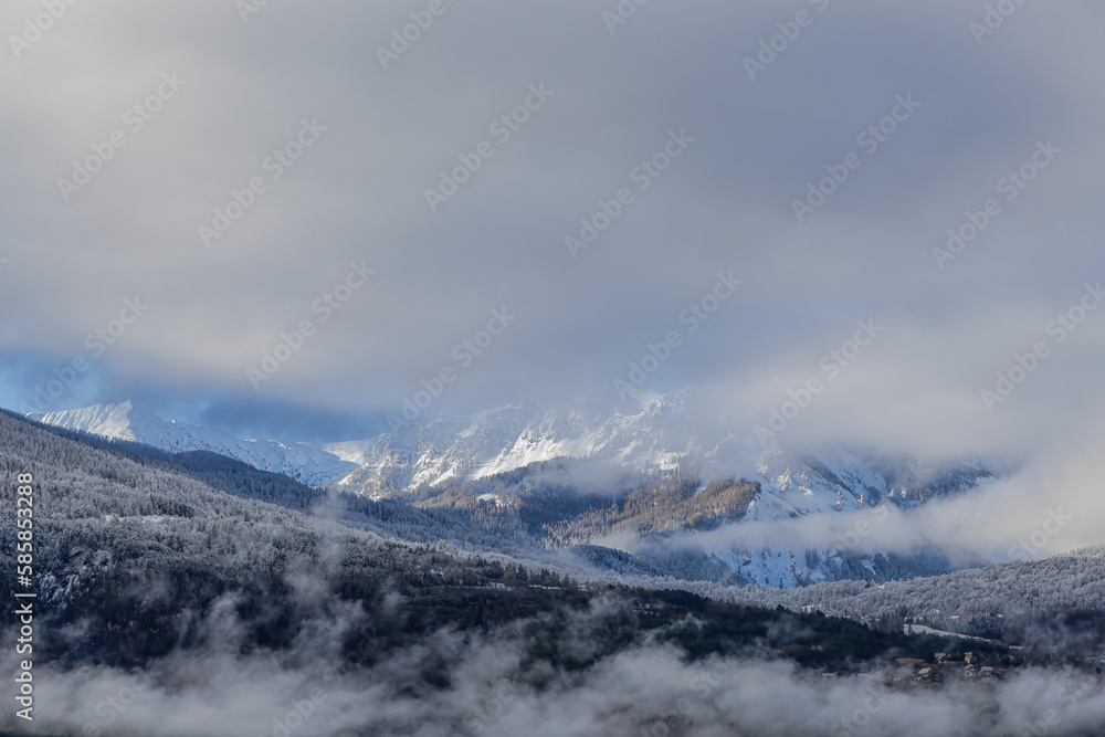 A scenic view of majestic snowy and foggy mountain with some frost on the top of the forest under a majestic blue sky