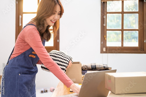 Young business woman working online e-commerce shopping at shop. Young woman seller prepare parcel box of product for deliver to customer. Online selling, e-commerce.SME business entrepreneurs ideas, © Fahng