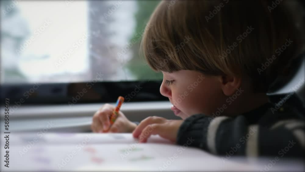One focused child doing school activity seated in a moving train by window. Little boy nose picking while studying on commute One focused child doing school activity seated in a moving train by window. Little boy nose picking while studying on commute