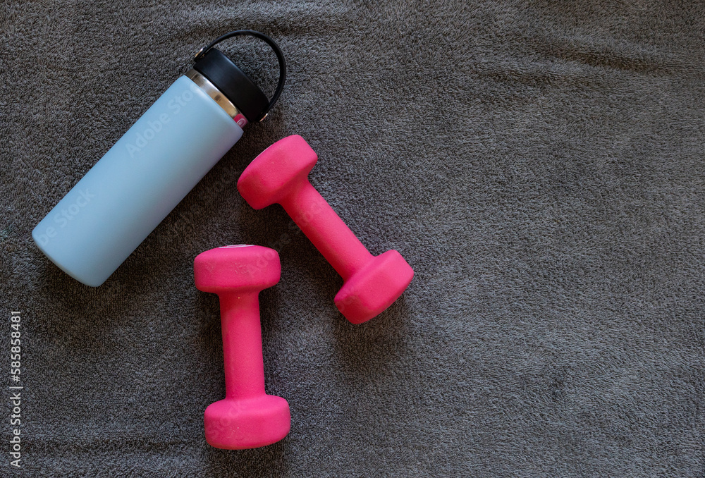 pale blue water bottle and set of dark pink hand weights on grey towel pale blue water bottle and set of dark pink hand weights on grey towel