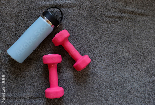 pale blue water bottle and set of dark pink hand weights on grey towel 