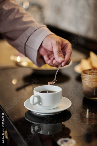 Hand of senior man putting spoon of brown sugar in cup of coffee