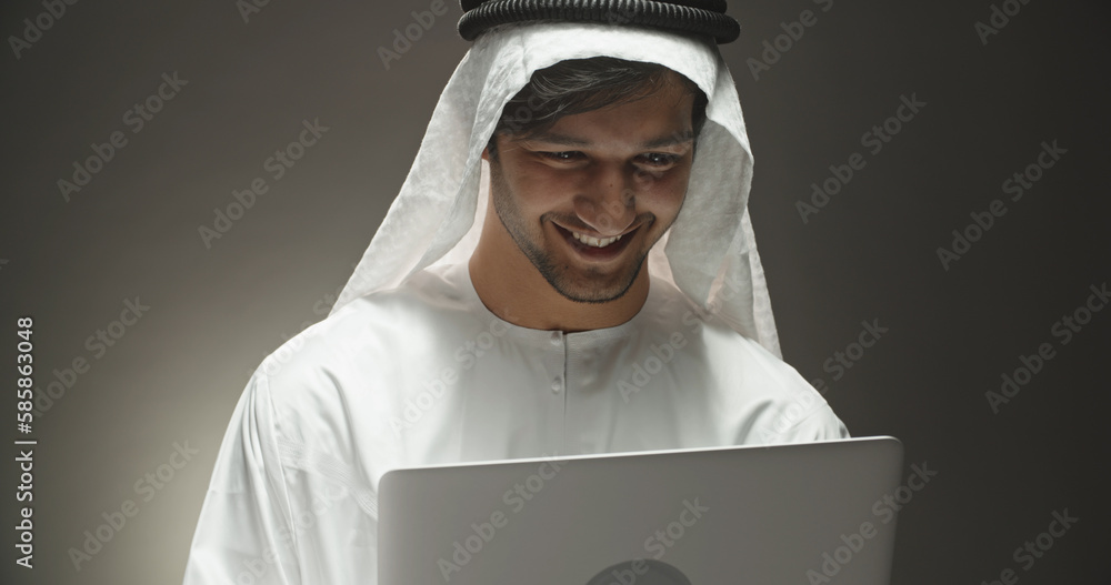 Close up shot of arab businessman surfing in internet using his laptop and positively smiling, isolated on black background close up Close up shot of arab businessman surfing in internet using his laptop and positively smiling, isolated on black background close up
