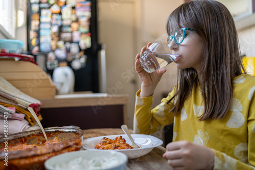 child girl is drinking water in kitchen at home