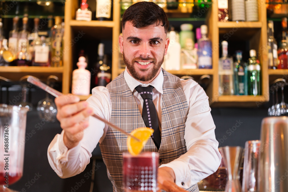 Young mixologist preparing a drink for his client with a special decoration. Concept: bartender, waiter, drink
