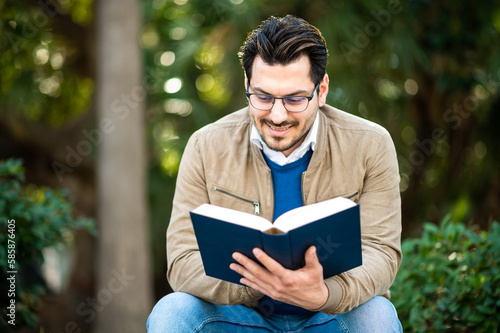 Male student reading a book on a bench outdoor