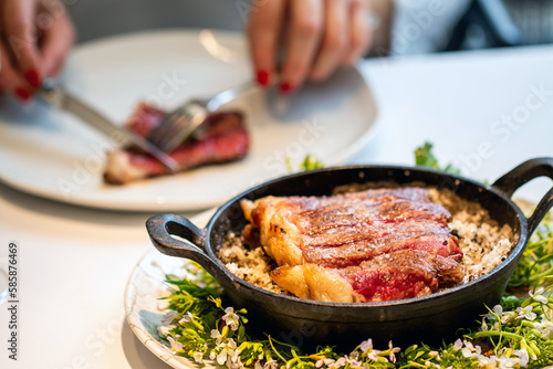 Appetizing wagyu sirloin steak in iron bowl with woman eating in background