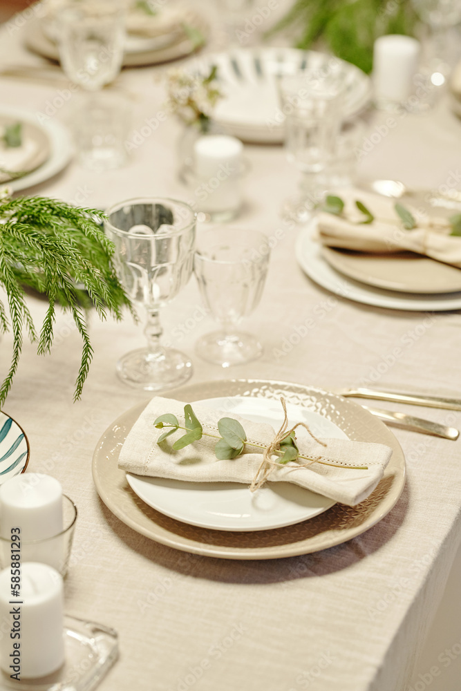 Part of dinner table with plates, candles, flutes and green plants served in living room or kitchen for family celebration of life event