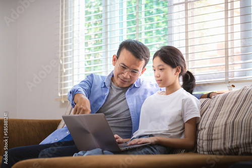 Asian father and daughter using laptop at home, People doing activities and family concepts