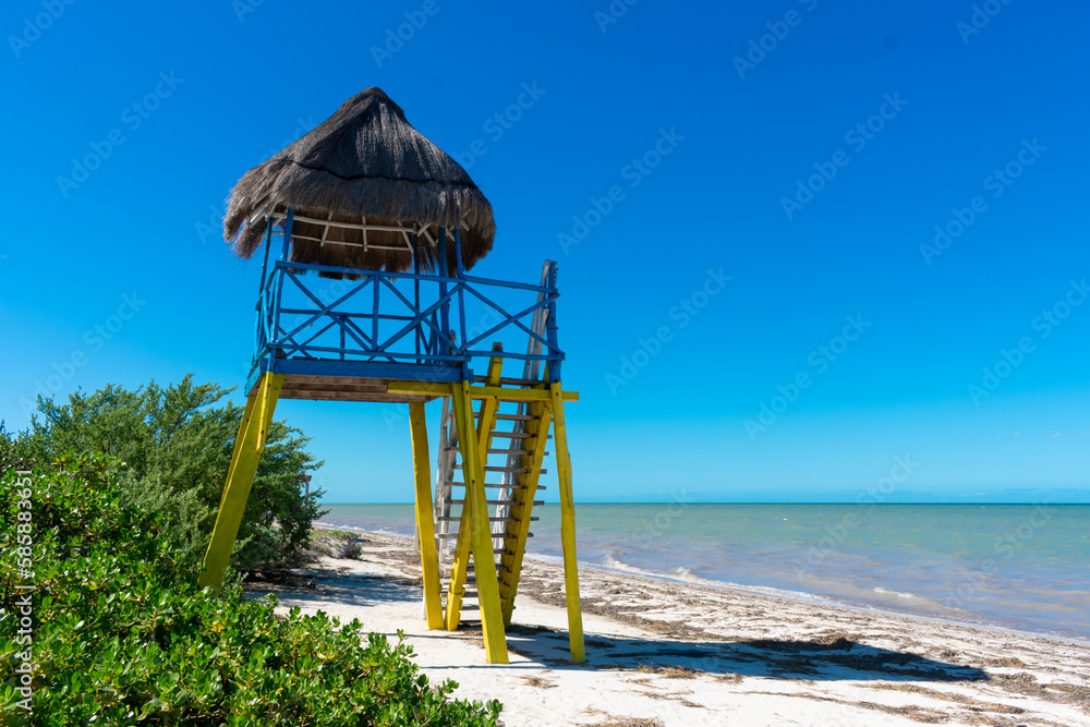 Playa de San Crisanto en Yucatán, torre de salvavidas azul y amarillo, en la playa, con el cielo azul y la arena blanca.