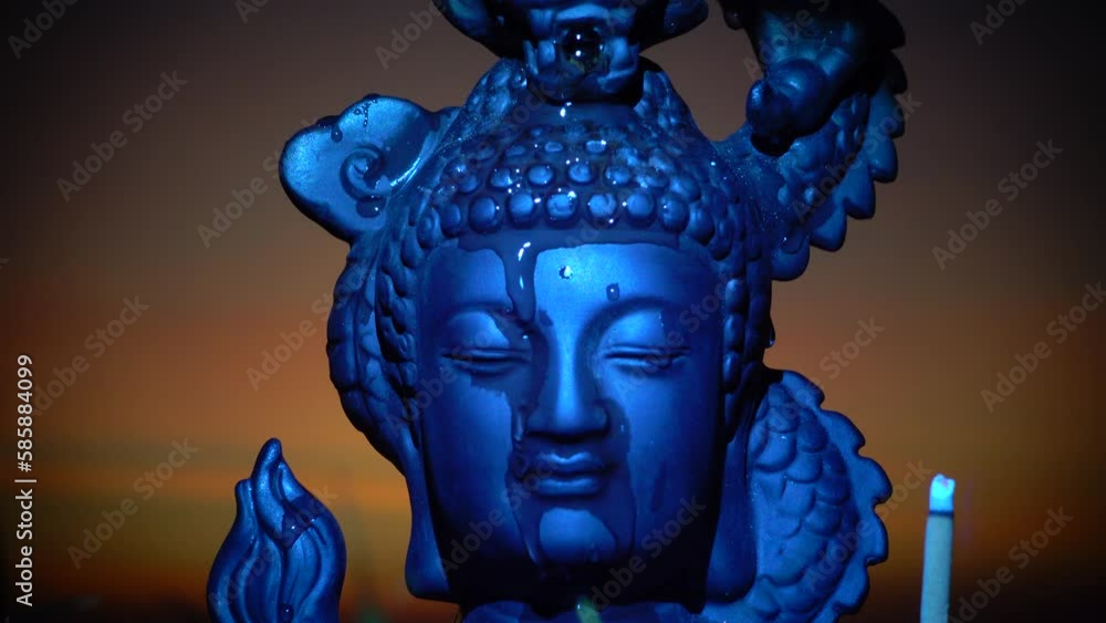The stone Head of the Buddha with closed eyes against the background of the sunset. Water flows down the head – a minifontane. The stone Head of the Buddha with closed eyes against the background of the sunset. Water flows down the head – a minifontane.