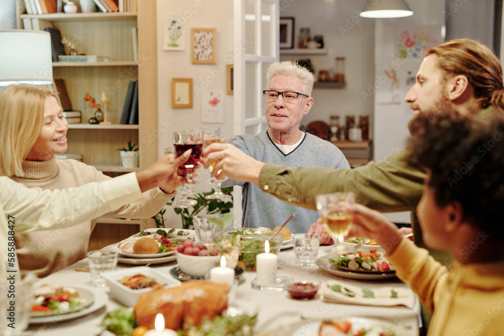 Group of family mambers clinking with glasses of homemade wine over table served with food and decorated with burning candles