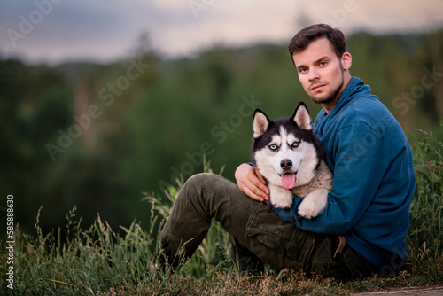 Portrait of a handsome young man and his pet dog Siberian Husky in nature.