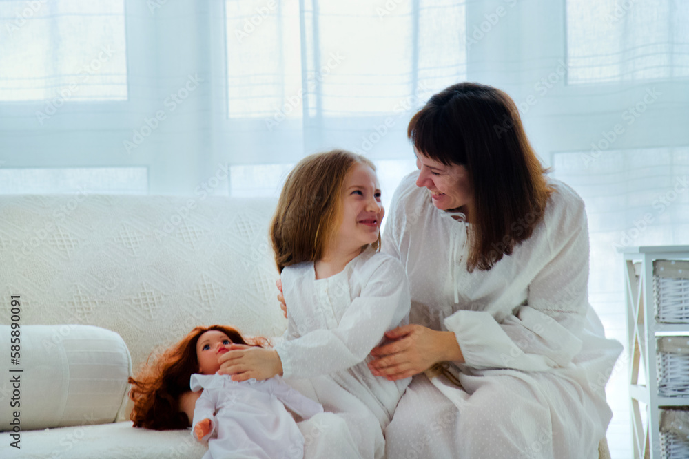 Fototapeta premium Portrait of happy family. Young mother and little daughter sits on a couch and having fun together at home.