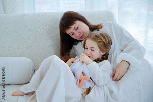 Portrait of happy family. Young mother and little daughter sits on a couch together at home.