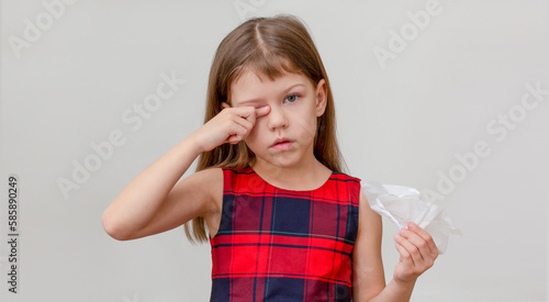 Fotografie Child scratching eye and holding napkin in hand showing allergy on white backgro