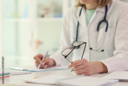 Doctor writes notes holding glasses at table in hospital