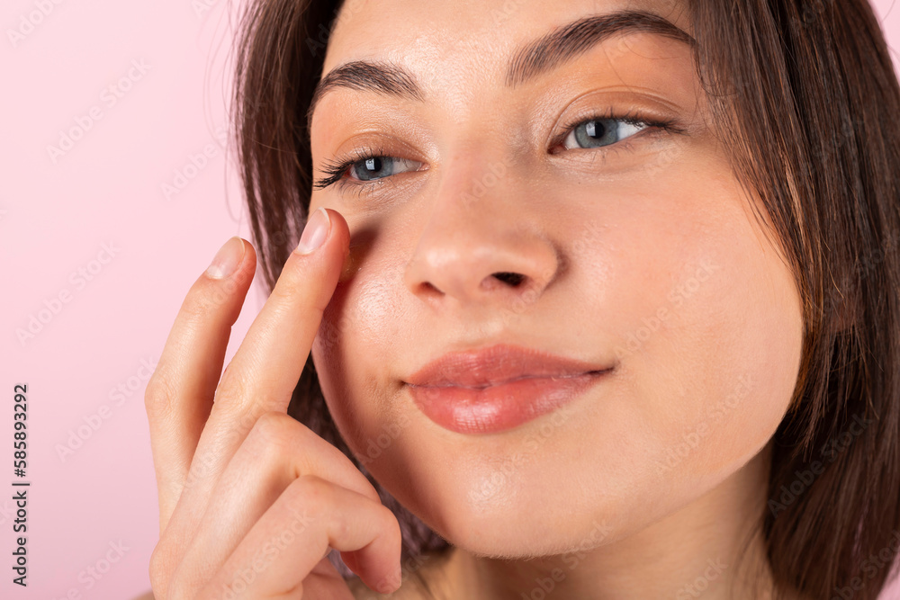 An attractive teenage girl wrapped only in a white towel is happily smiling and using a new face cream on her face. isolated on a pink background. Close-up. An attractive teenage girl wrapped only in a white towel is happily smiling and using a new face cream on her face. isolated on a pink background. Close-up.
