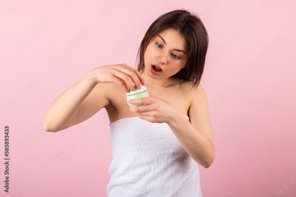 Excited and surprised teenage girl wrapped only in a white towel is opening her new jar of cream. isolated on a pink background. Excited and surprised teenage girl wrapped only in a white towel is opening her new jar of cream. isolated on a pink background.