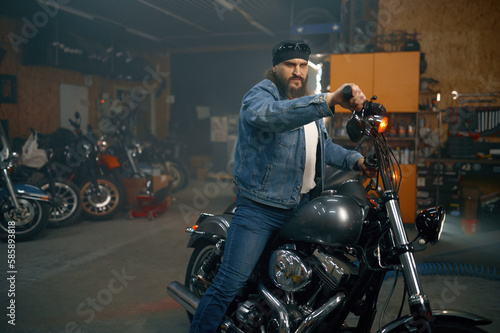 Handsome bearded man testing new motorbike in garage store