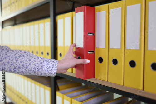 Hand of woman taking red ring binder among yellow in row