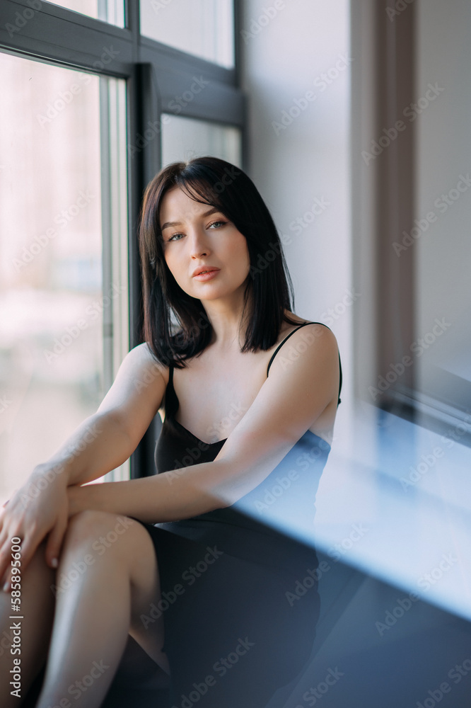 A girl with shoulder-length black hair is sitting by a huge window 4556. A girl with shoulder-length black hair is sitting by a huge window 4556.