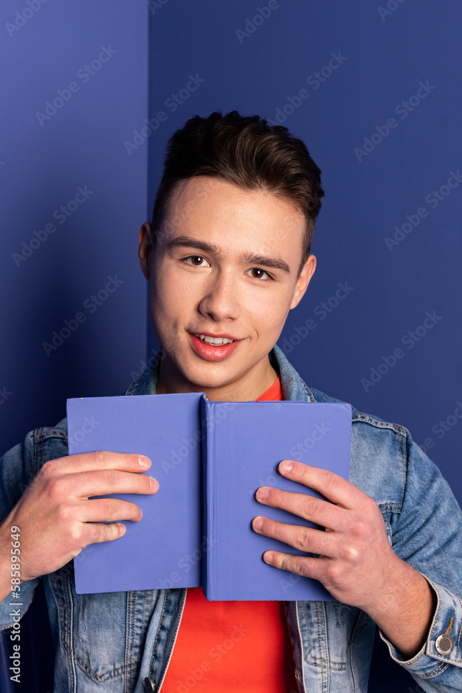 Portrait of a handsome young man in denim clothes holding a book and posing in a room where everything is blue or purple, a room that is completely painted in one color. Portrait of a handsome young man in denim clothes holding a book and posing in a room where everything is blue or purple, a room that is completely painted in one color.