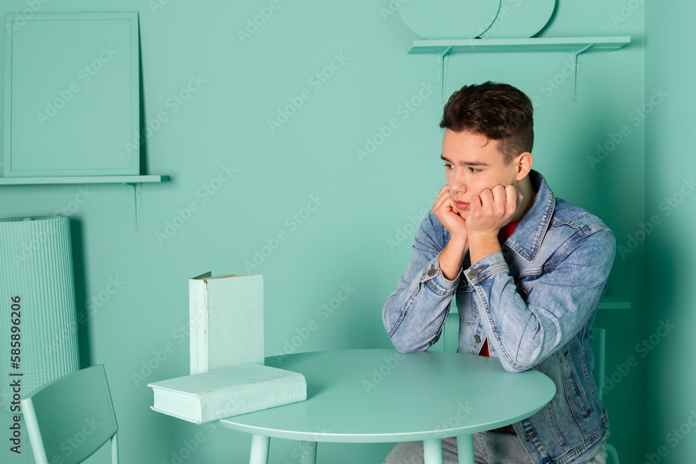 Portrait of a handsome young man in denim clothes posing in a room where everything is colored in mint, a room that is completely painted in one color. looking at the books. Portrait of a handsome young man in denim clothes posing in a room where everything is colored in mint, a room that is completely painted in one color. looking at the books.