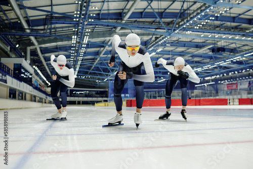 Canvas-taulu Young male ice skater in sports uniform and two more sportsmen behind him slidin